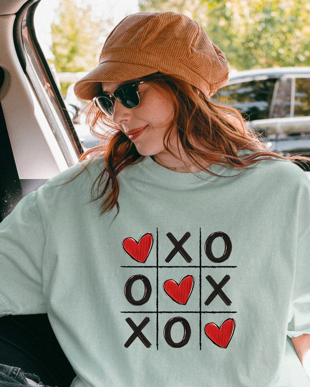 Person sitting in a car wearing a light green t-shirt with a graphic design, sitting in a car.