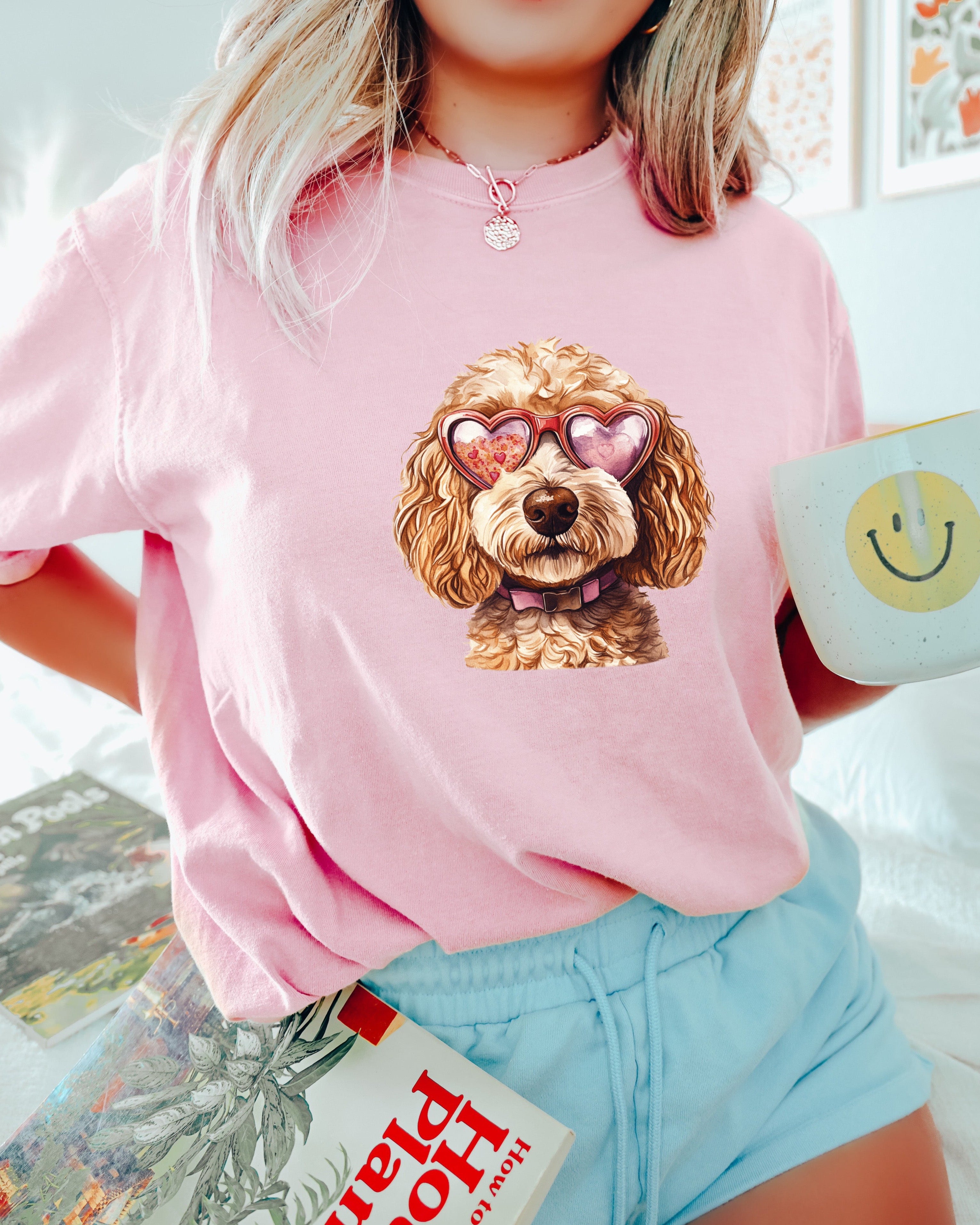 Person wearing a pink sweatshirt with a dog graphic, holding a mug and book.