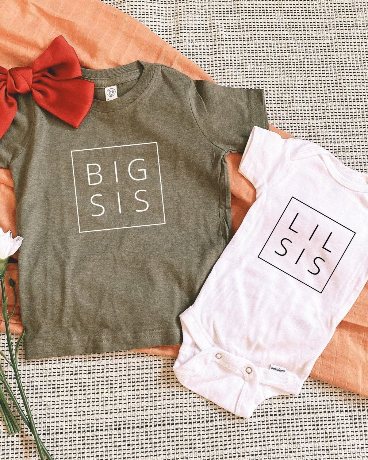 Olive green "BIG SIS" t-shirt and white "LIL SIS" onesie for pregnancy announcement.