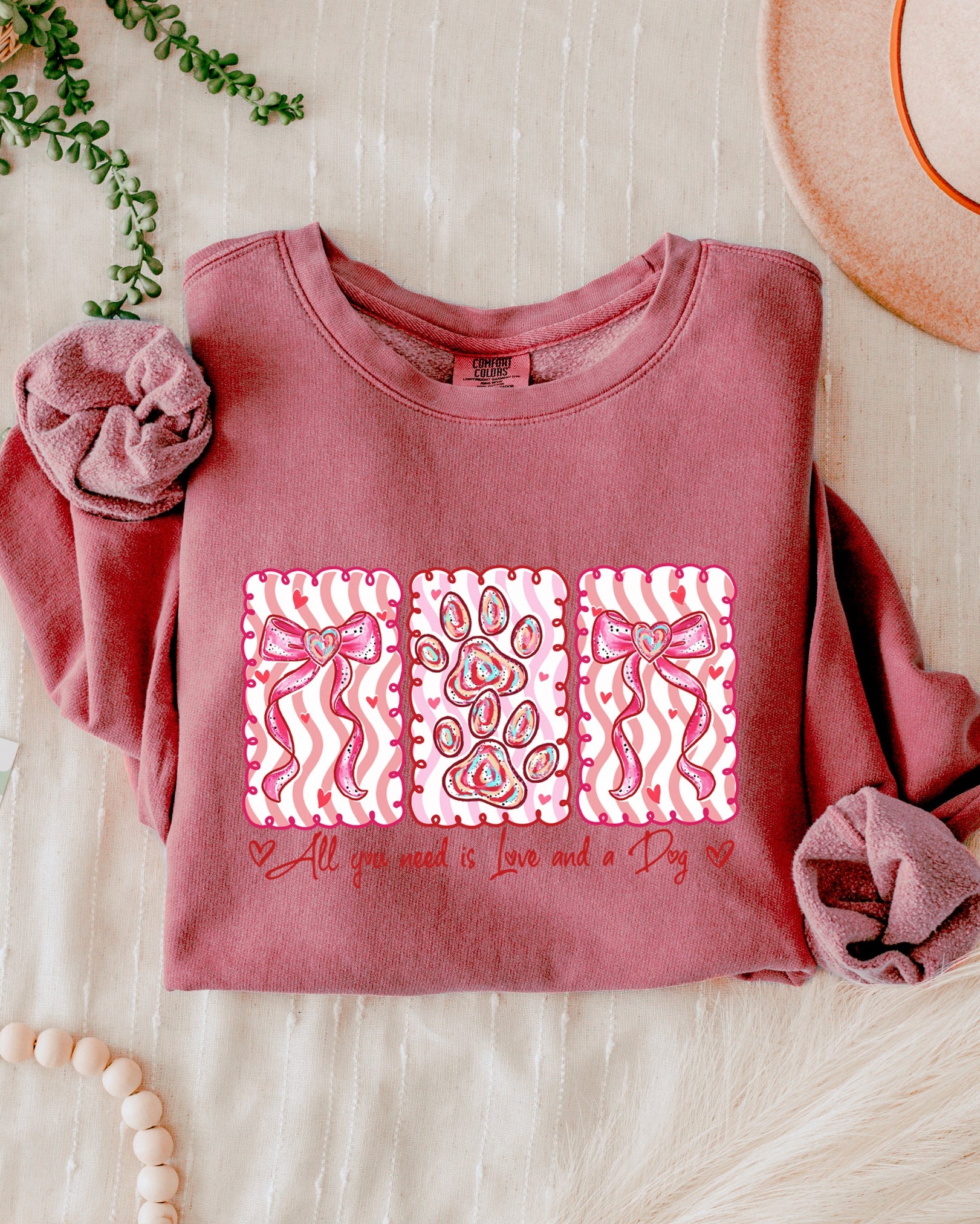 Pink sweatshirt with decorative patterns and text on a light wooden surface with a hat and decorative items.