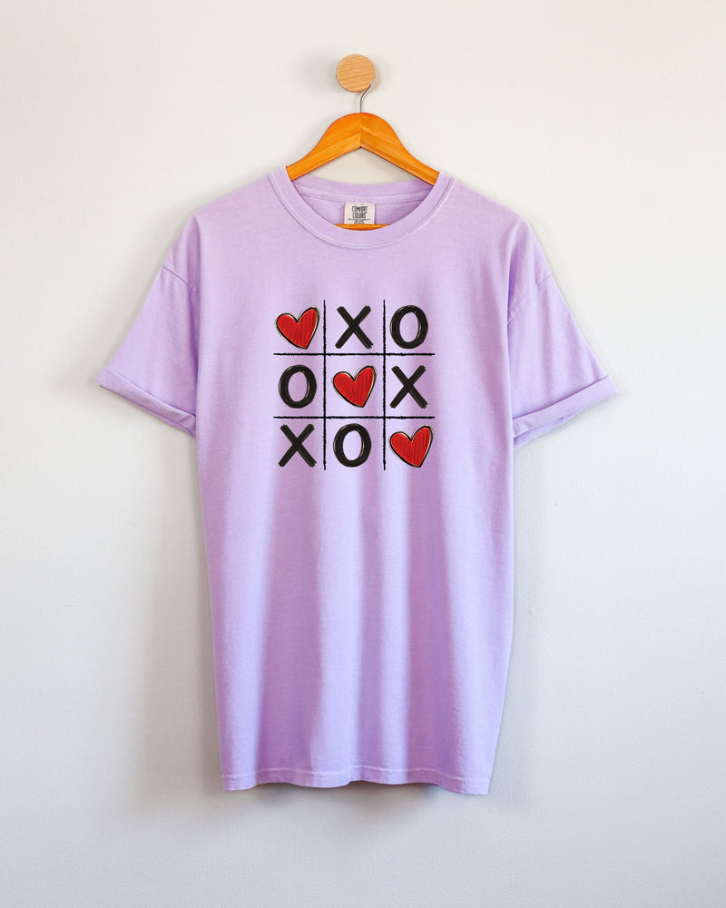 Lavender t-shirt with a tic-tac-toe design featuring hearts and 'XO' on a white background.