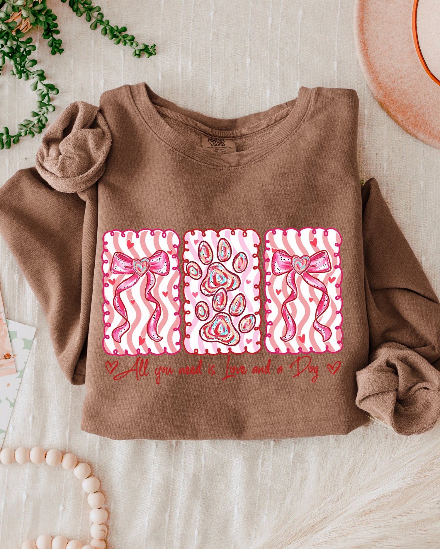 Brown sweatshirt with pink and white pattern and text on a light wooden surface.