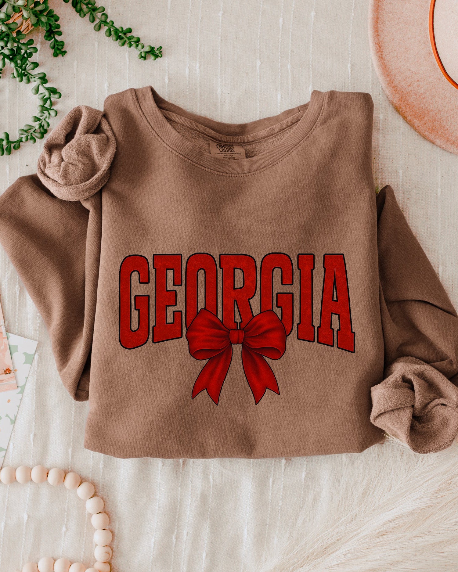 Brown sweatshirt with 'Georgia' and a red bow on a light wooden surface.