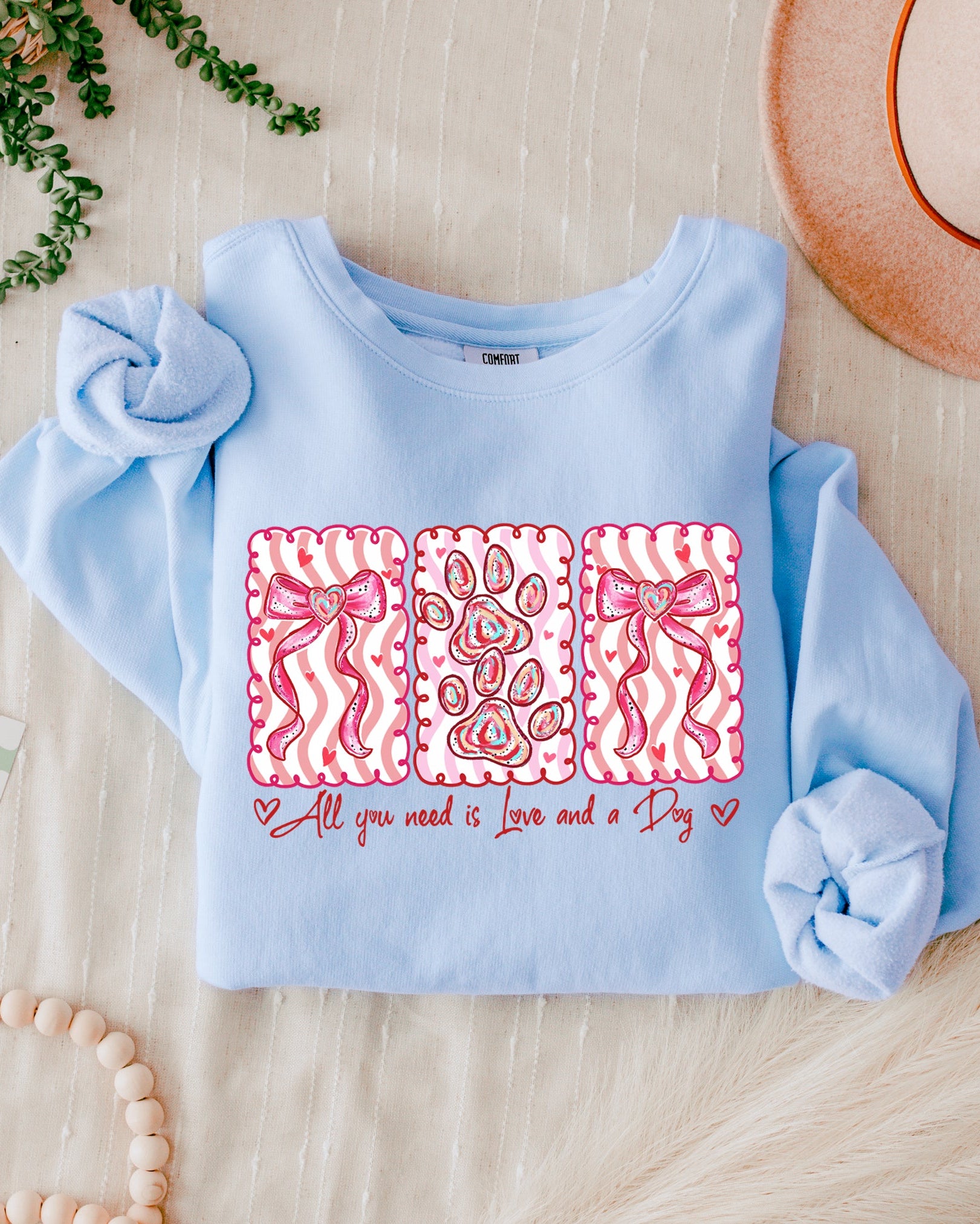 Light blue baby sweater with pink designs and text on a wooden surface.
