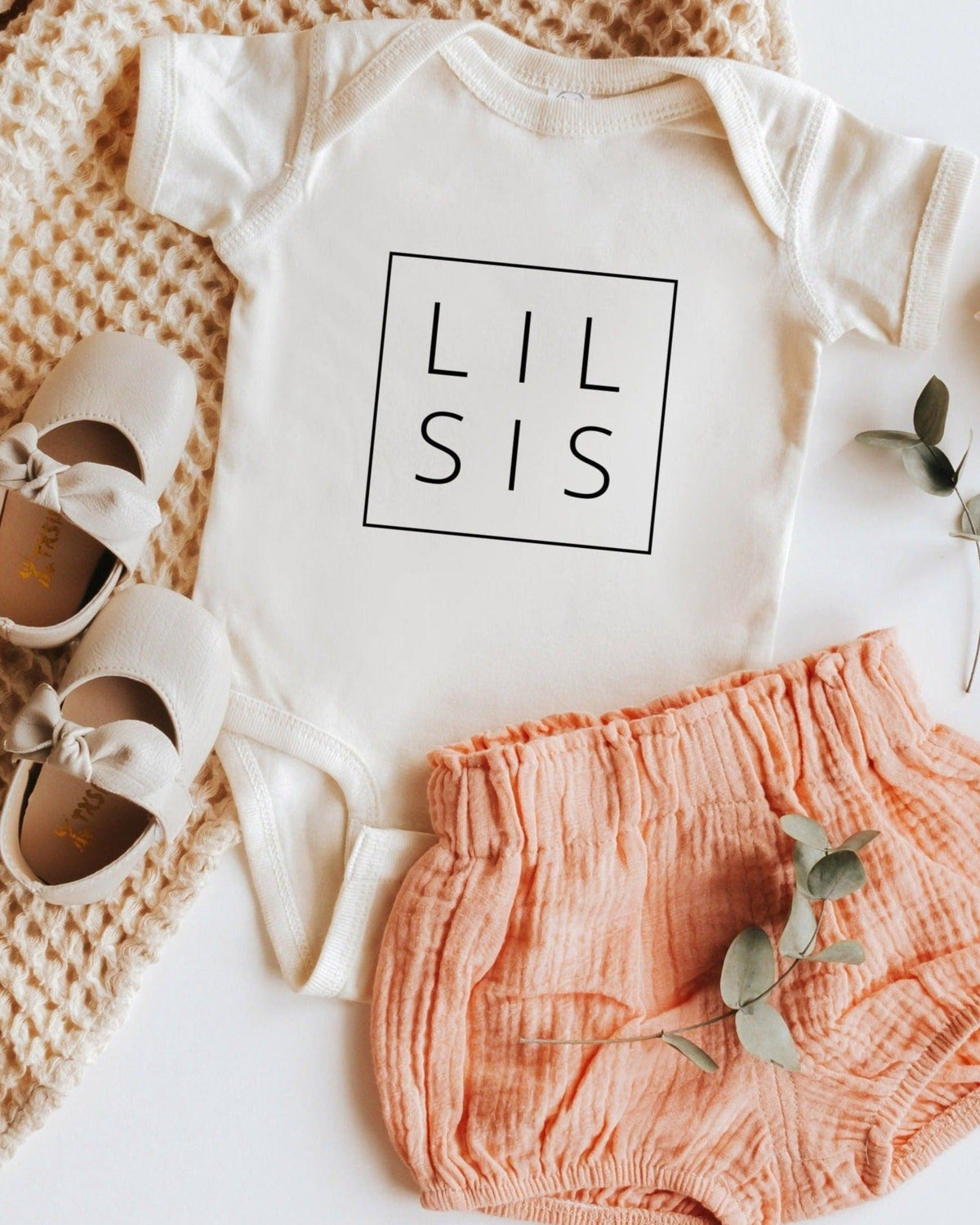 Cream "LIL SIS" baby onesie with short sleeves, snap closure, paired with peach bloomers and shoes.